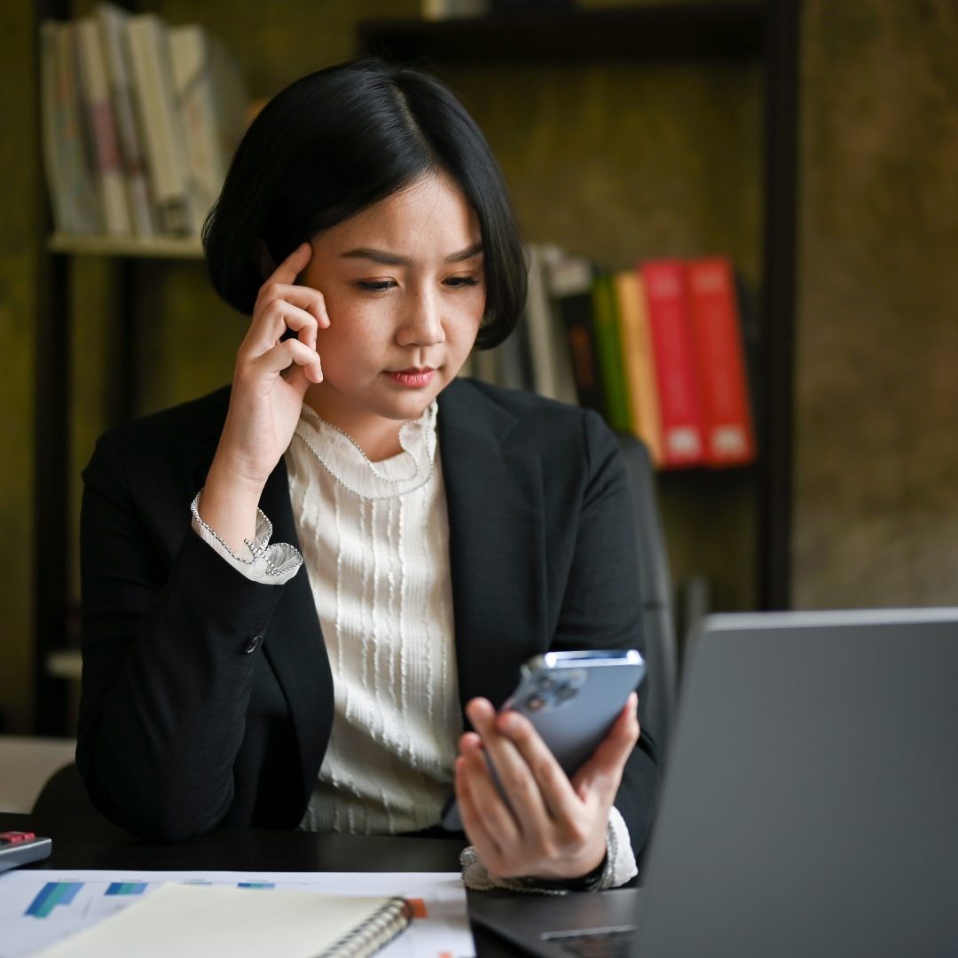 thoughtful-asian-businesswoman-looking-her-phone-screen-pensively-thinking (1)